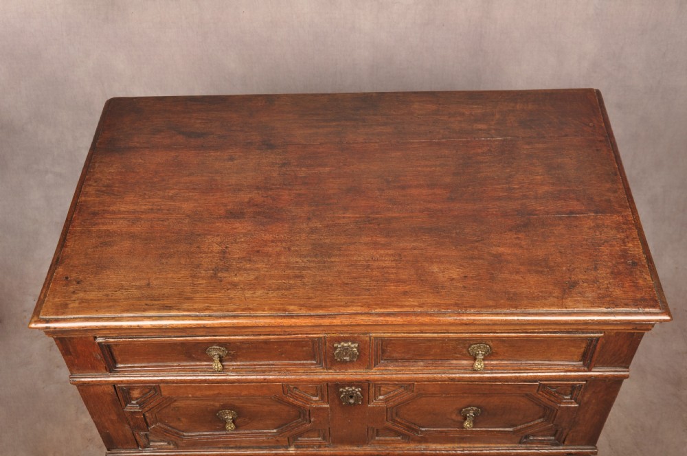 A 17th-century Charles II solid oak chest of drawers featuring geometric applied mouldings and brass teardrop handles. View IX