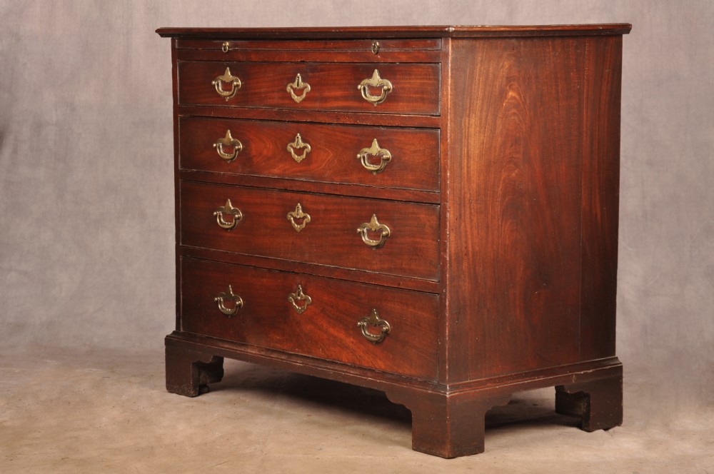 An early eighteenth-century mahogany chest of drawers featuring four graduated drawers, brass handles, a brushing slide, and bracket feet.