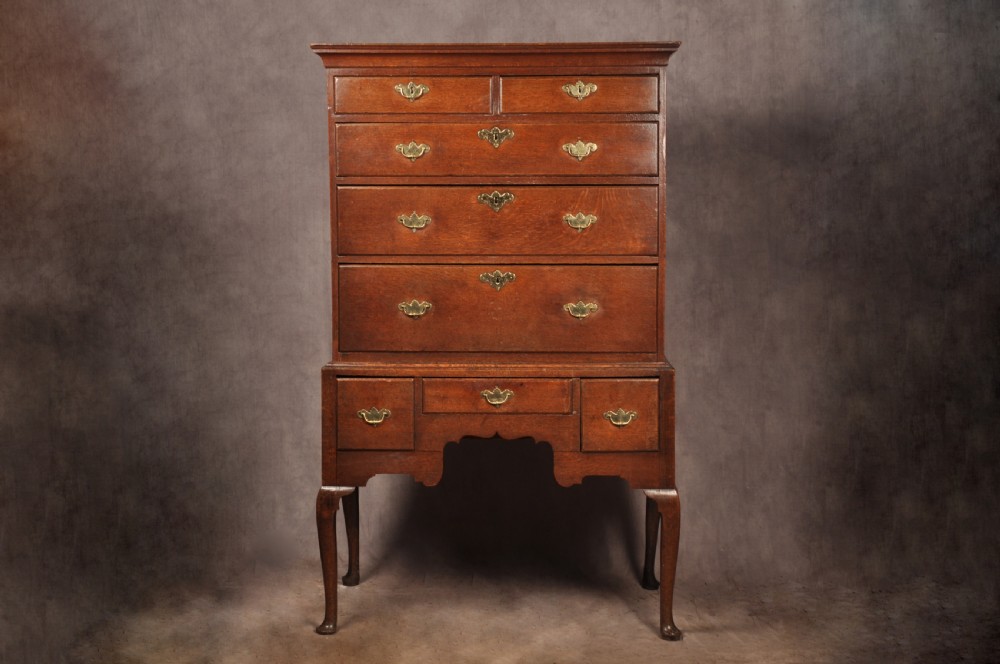 An 18th-century George I oak chest on stand featuring multiple graduated drawers with brass handles, resting on shaped cabriole legs.