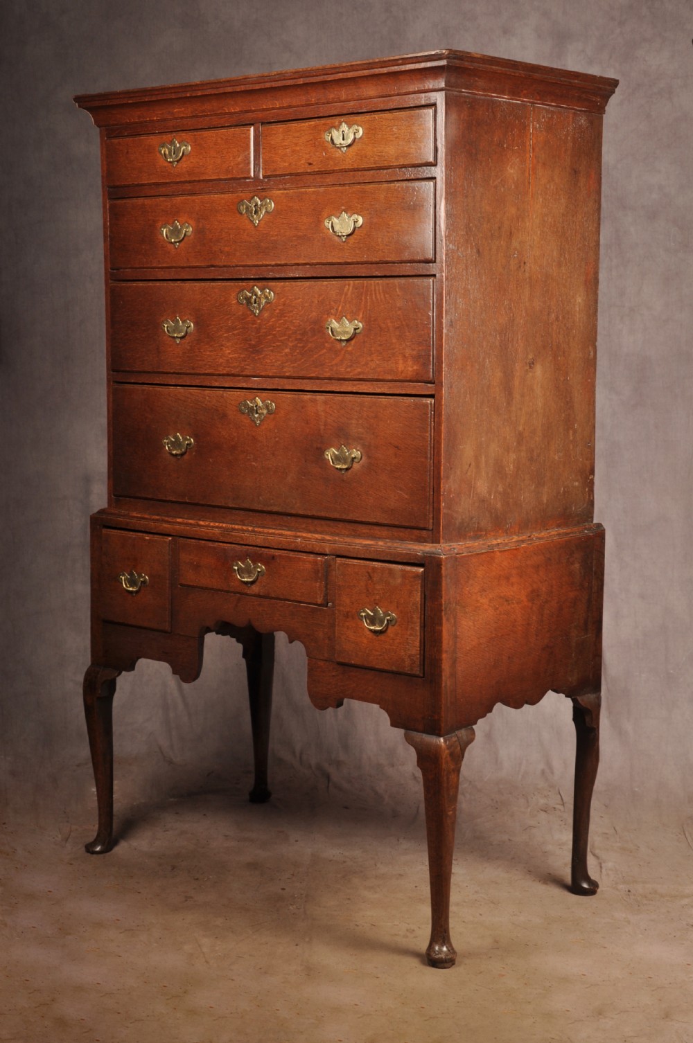 An 18th-century George I oak chest on stand featuring multiple graduated drawers with brass handles, resting on shaped cabriole legs. View VI