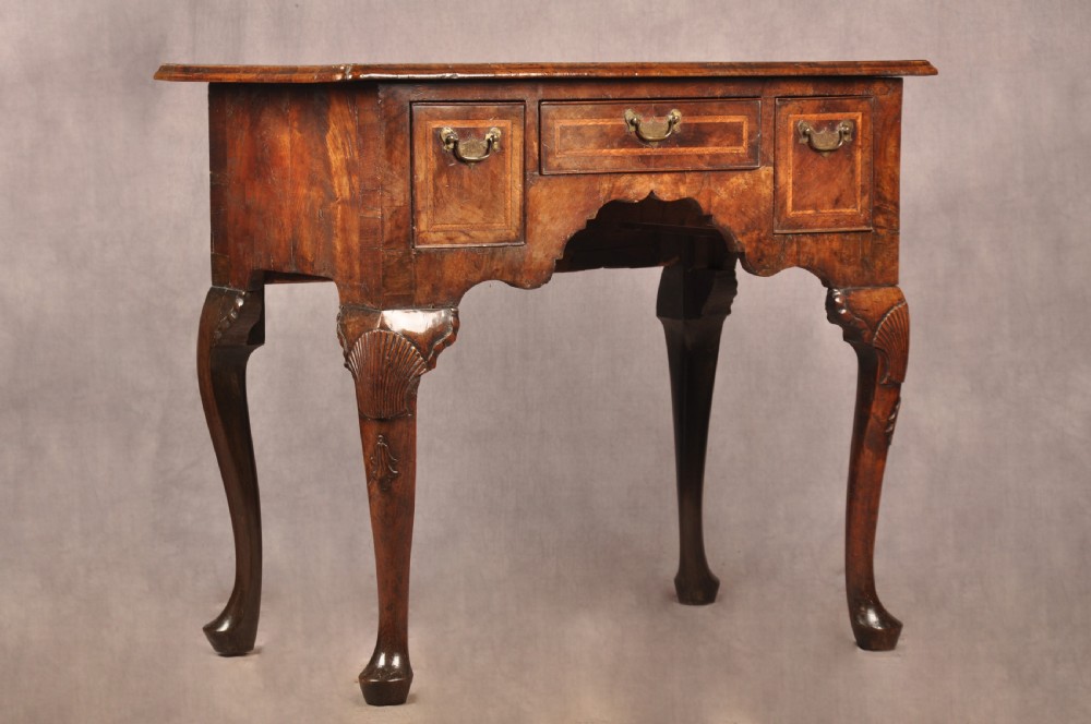 An early 18th century walnut lowboy featuring three drawers with brass handles, a shaped apron, and shell-carved cabriole legs. View II