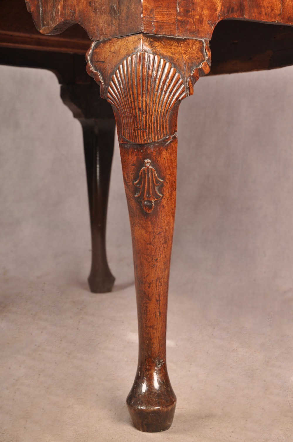 An early 18th century walnut lowboy featuring three drawers with brass handles, a shaped apron, and shell-carved cabriole legs. View VI