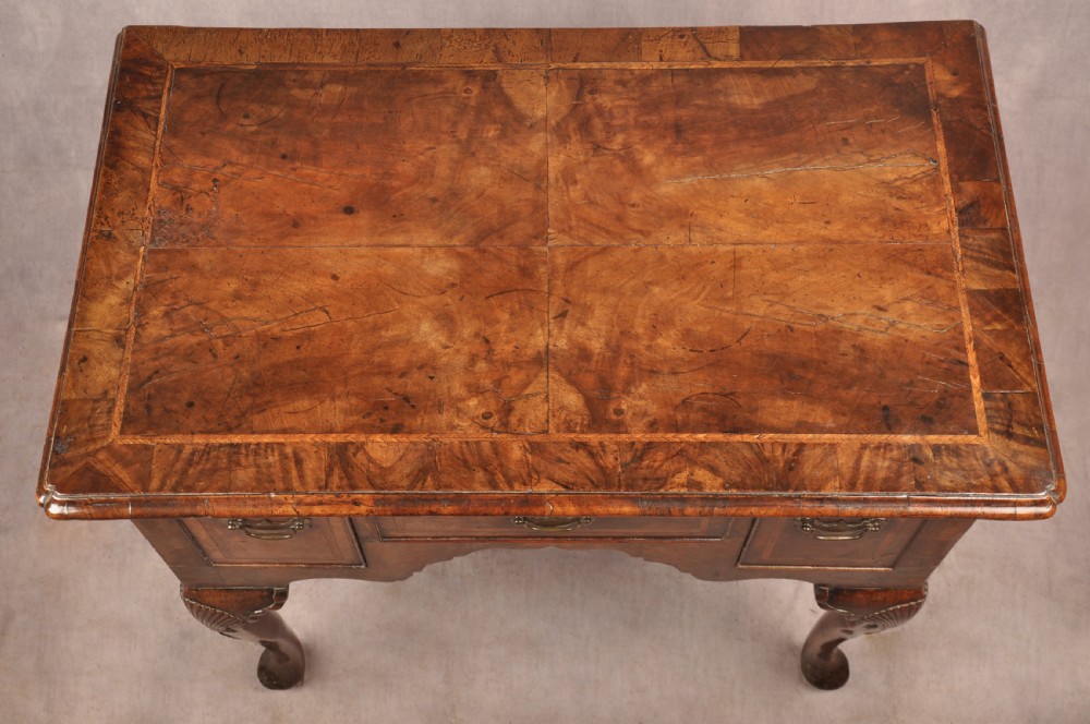 An early 18th century walnut lowboy featuring three drawers with brass handles, a shaped apron, and shell-carved cabriole legs. View VIII