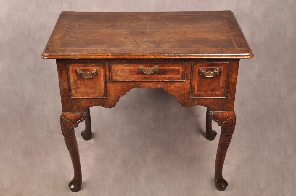 An early 18th century walnut lowboy featuring three drawers with brass handles, a shaped apron, and shell-carved cabriole legs. View XIV