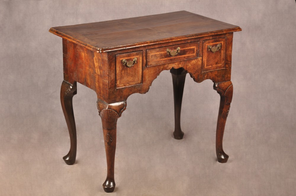 An early 18th century walnut lowboy featuring three drawers with brass handles, a shaped apron, and shell-carved cabriole legs. View XV