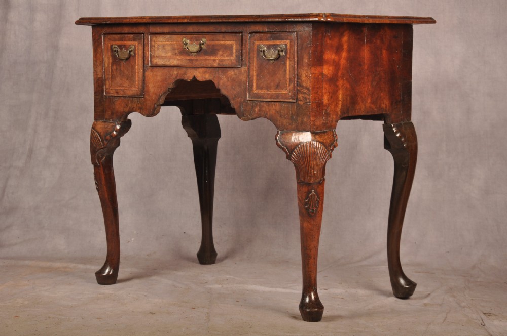 An early 18th century walnut lowboy featuring three drawers with brass handles, a shaped apron, and shell-carved cabriole legs. View XVI