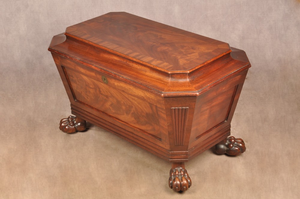 A Regency flame mahogany sarcophagus-shaped wine cooler featuring a hinged stepped lid, reeded corners, and carved paw feet.