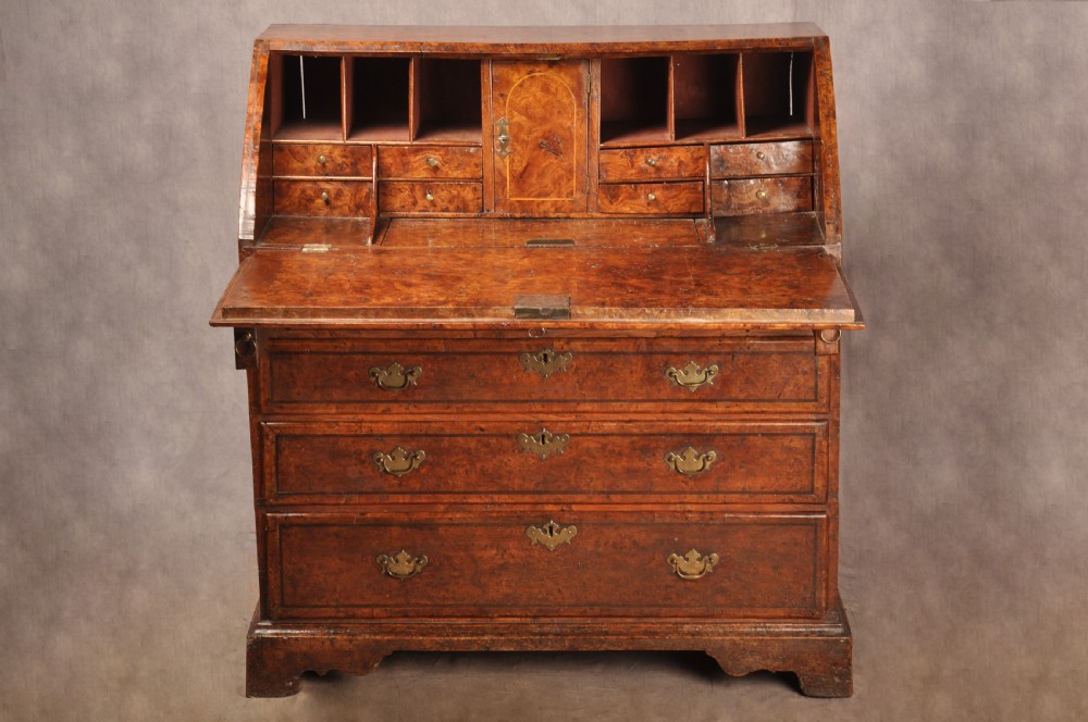 An early 18th-century burr elm slant-front writing bureau featuring figured wood grain, brass drop handles, and bracket feet. View V