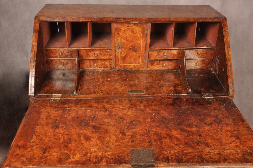 An early 18th-century burr elm slant-front writing bureau featuring figured wood grain, brass drop handles, and bracket feet. View VI