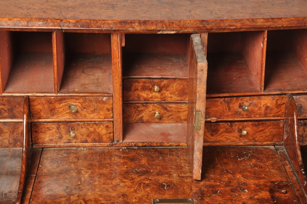An early 18th-century burr elm slant-front writing bureau featuring figured wood grain, brass drop handles, and bracket feet. View X