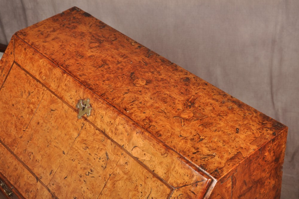 An early 18th-century burr elm slant-front writing bureau featuring figured wood grain, brass drop handles, and bracket feet. View XVIII
