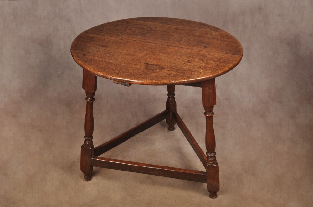 An 18th-century circular timber cricket table with three turned legs connected by a low triangular stretcher.