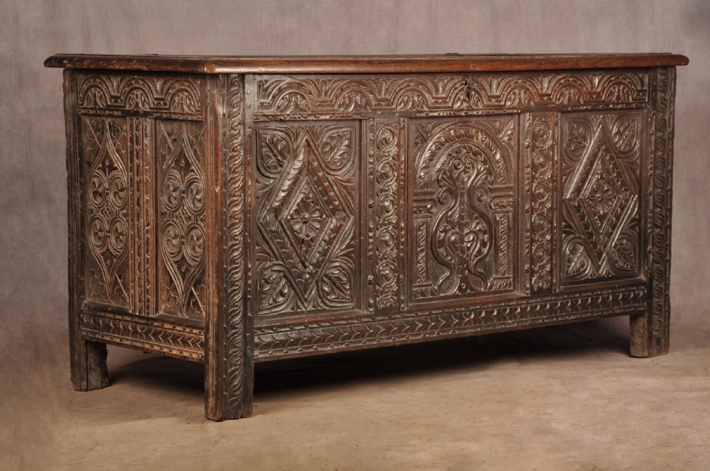 A 17th-century carved dark oak coffer featuring intricate geometric lozenge panels, an arched central carving, and a flat hinged lid.