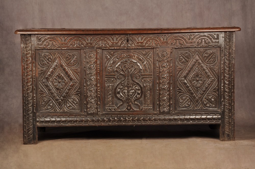 A 17th-century carved dark oak coffer featuring intricate geometric lozenge panels, an arched central carving, and a flat hinged lid. View II