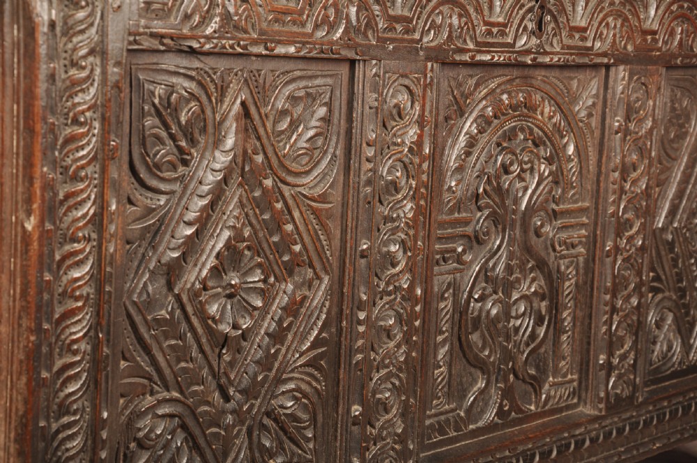 A 17th-century carved dark oak coffer featuring intricate geometric lozenge panels, an arched central carving, and a flat hinged lid. View V