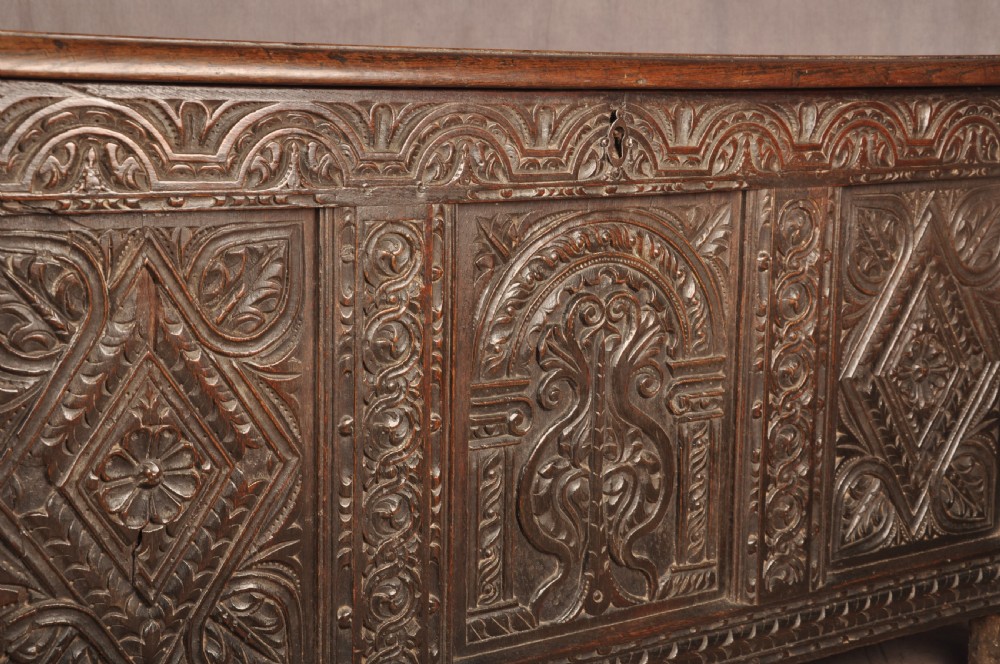 A 17th-century carved dark oak coffer featuring intricate geometric lozenge panels, an arched central carving, and a flat hinged lid. View VI