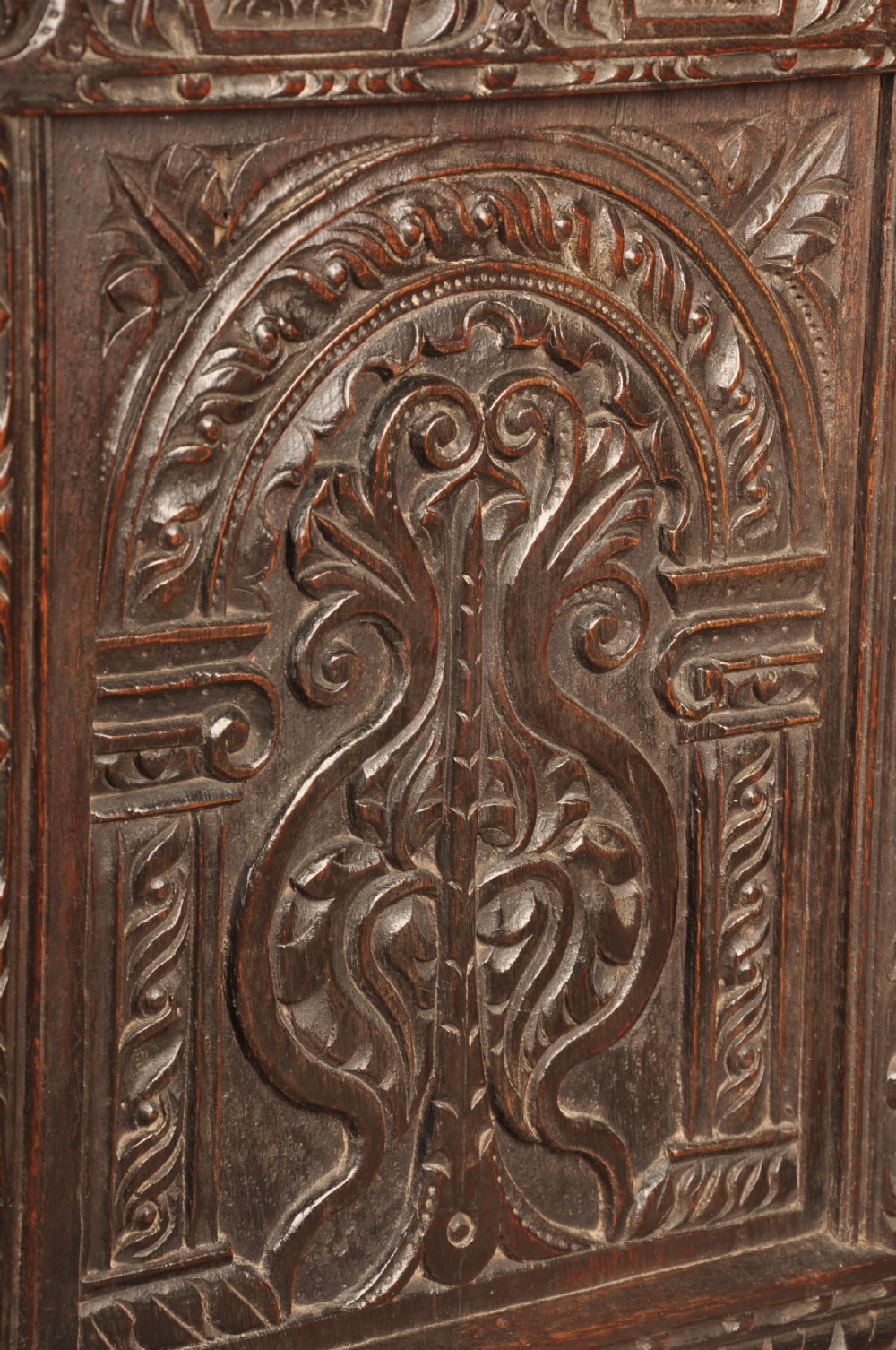 A 17th-century carved dark oak coffer featuring intricate geometric lozenge panels, an arched central carving, and a flat hinged lid. View VII