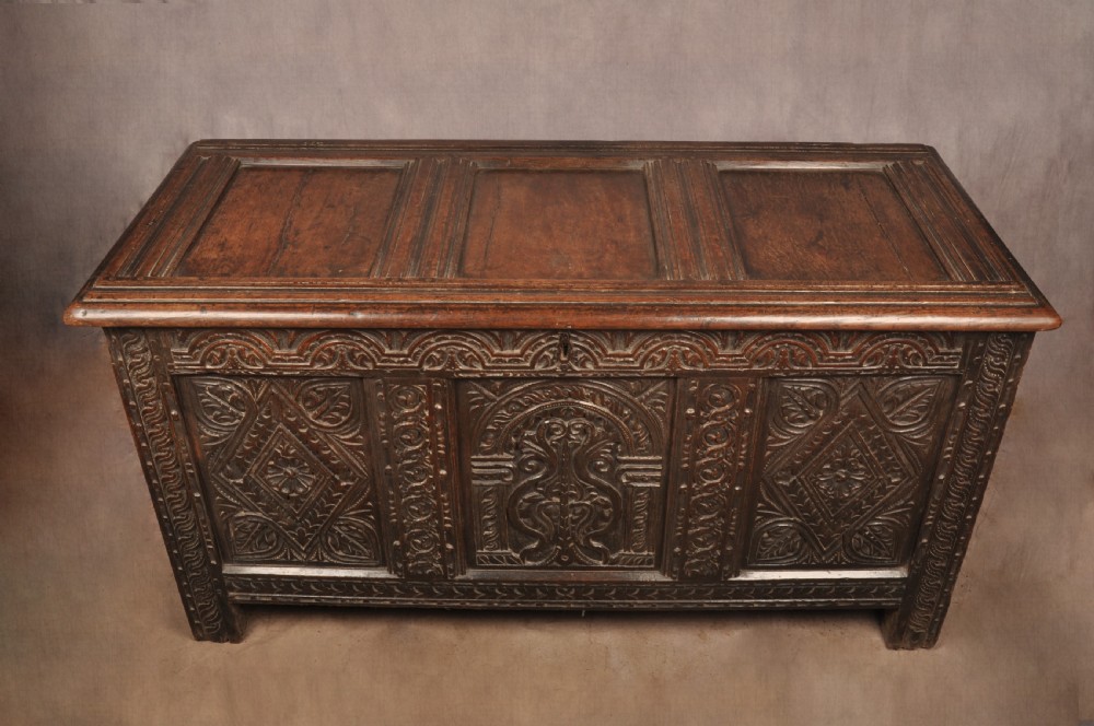 A 17th-century carved dark oak coffer featuring intricate geometric lozenge panels, an arched central carving, and a flat hinged lid. View VIII