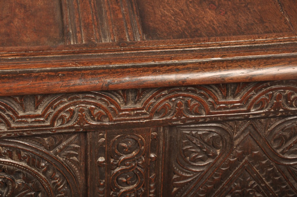 A 17th-century carved dark oak coffer featuring intricate geometric lozenge panels, an arched central carving, and a flat hinged lid. View IX