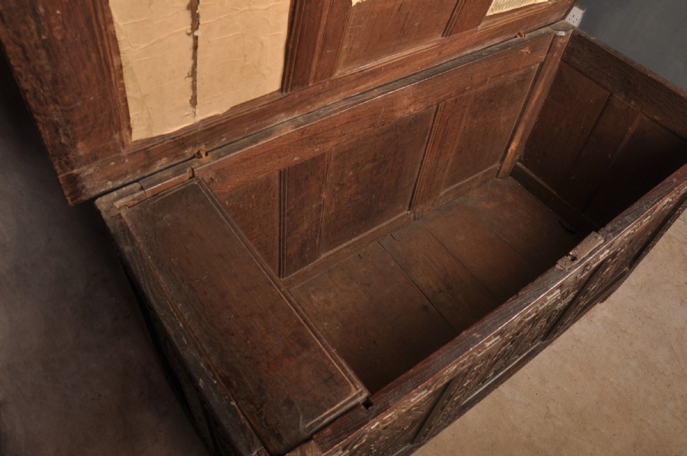 A 17th-century carved dark oak coffer featuring intricate geometric lozenge panels, an arched central carving, and a flat hinged lid. View X