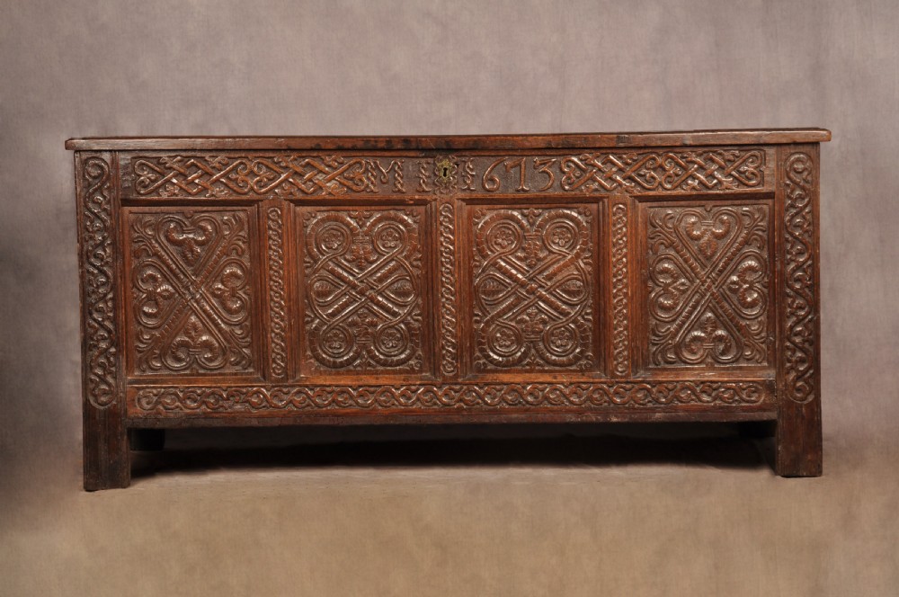 A dark oak 17th-century coffer featuring four carved relief panels, a carved top frieze with an inscribed date, and a hinged lid.