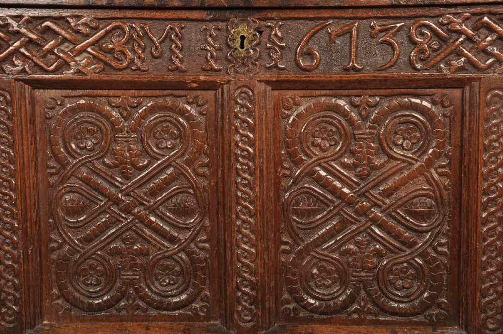A dark oak 17th-century coffer featuring four carved relief panels, a carved top frieze with an inscribed date, and a hinged lid. View II