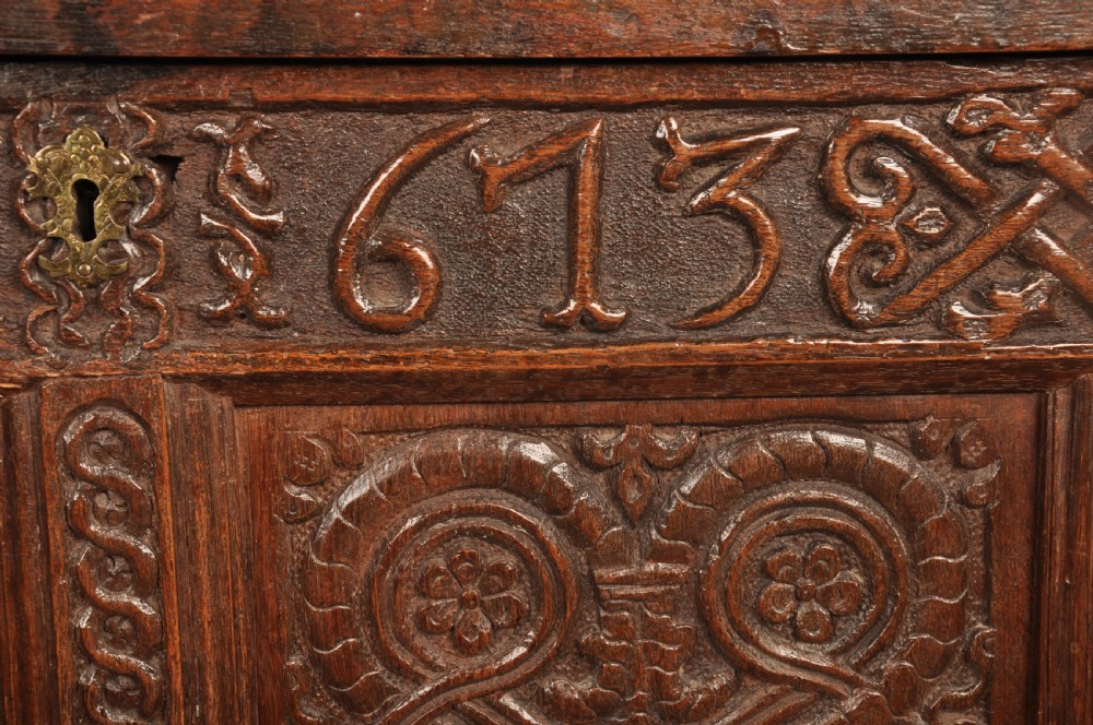 A dark oak 17th-century coffer featuring four carved relief panels, a carved top frieze with an inscribed date, and a hinged lid. View V