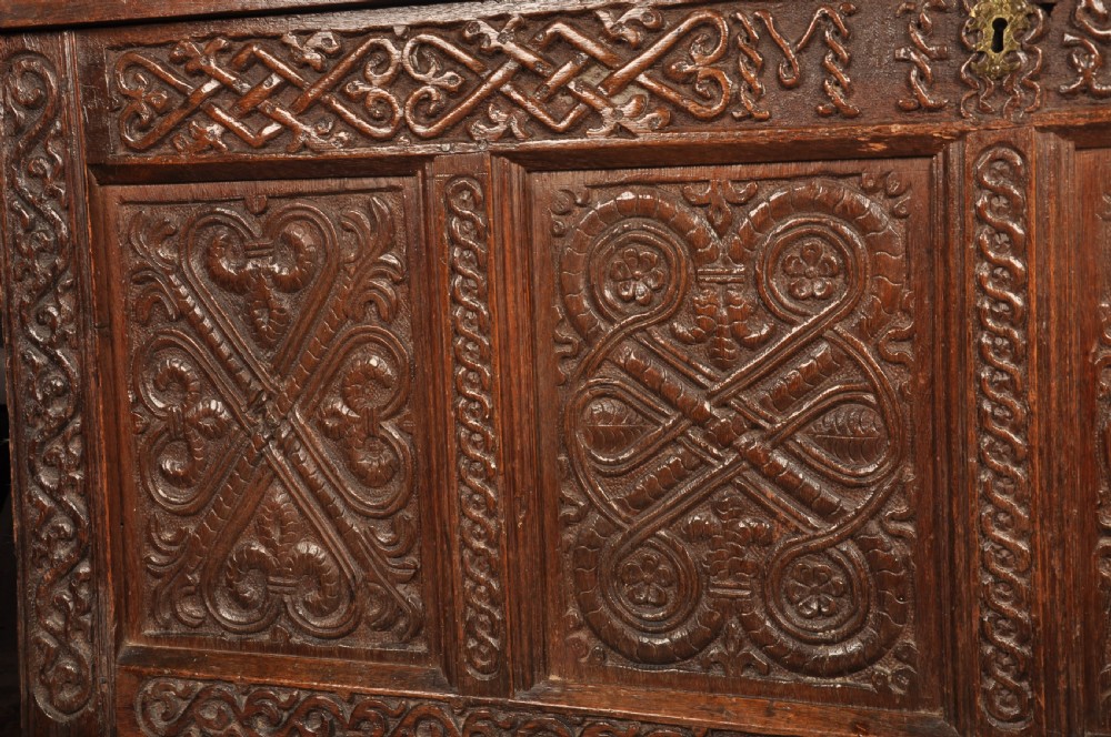 A dark oak 17th-century coffer featuring four carved relief panels, a carved top frieze with an inscribed date, and a hinged lid. View VI