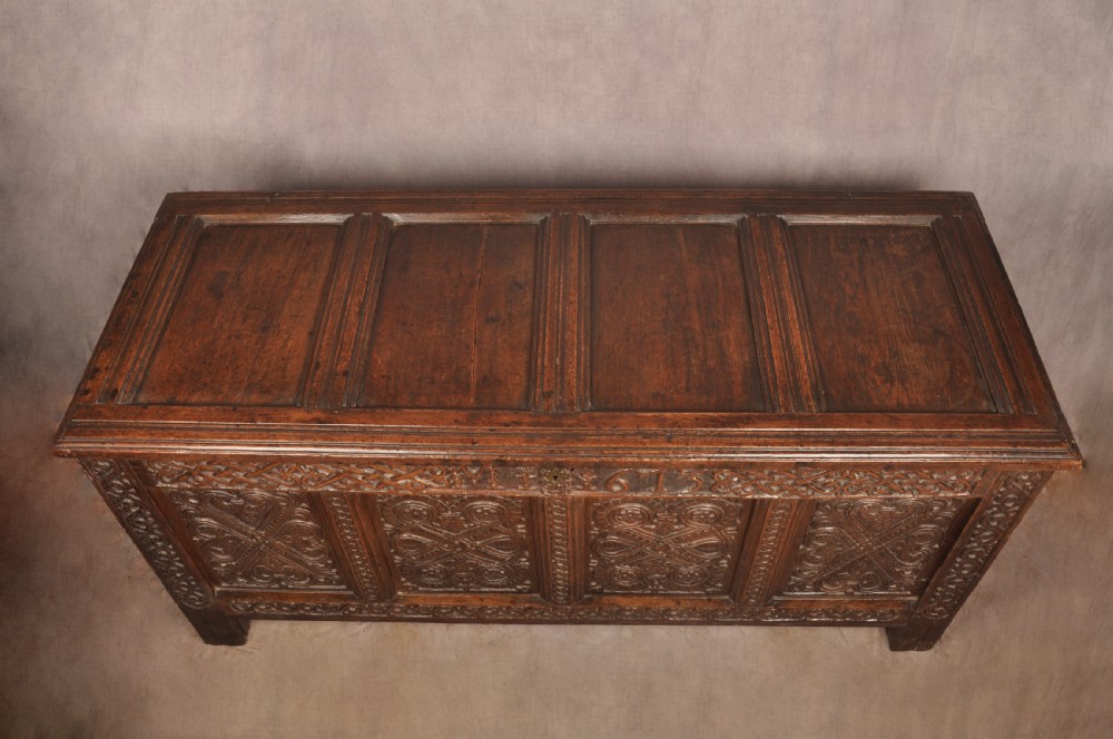 A dark oak 17th-century coffer featuring four carved relief panels, a carved top frieze with an inscribed date, and a hinged lid. View VII