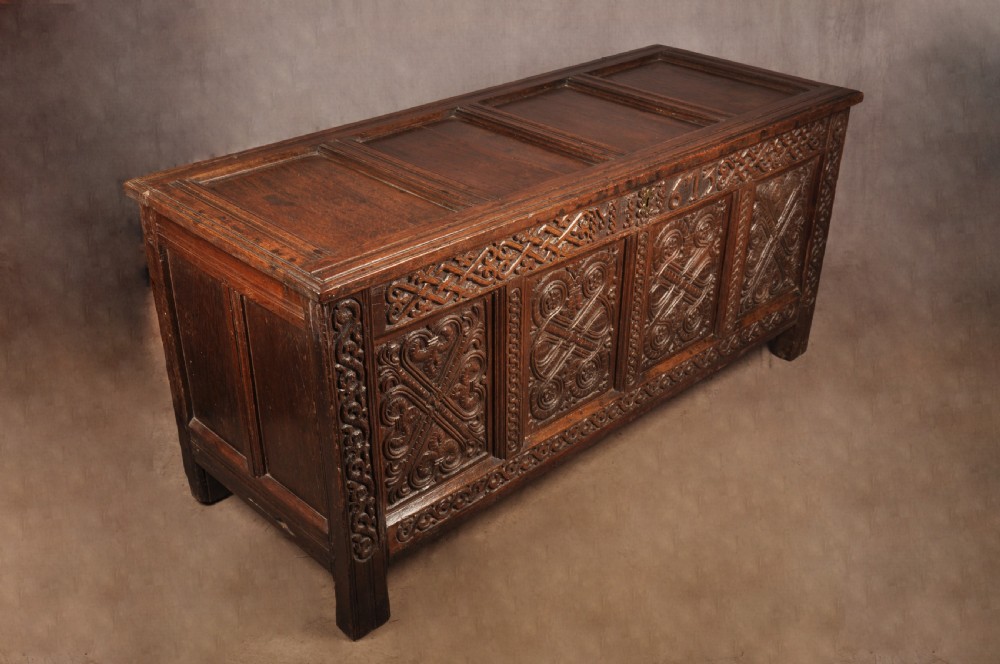A dark oak 17th-century coffer featuring four carved relief panels, a carved top frieze with an inscribed date, and a hinged lid. View VIII