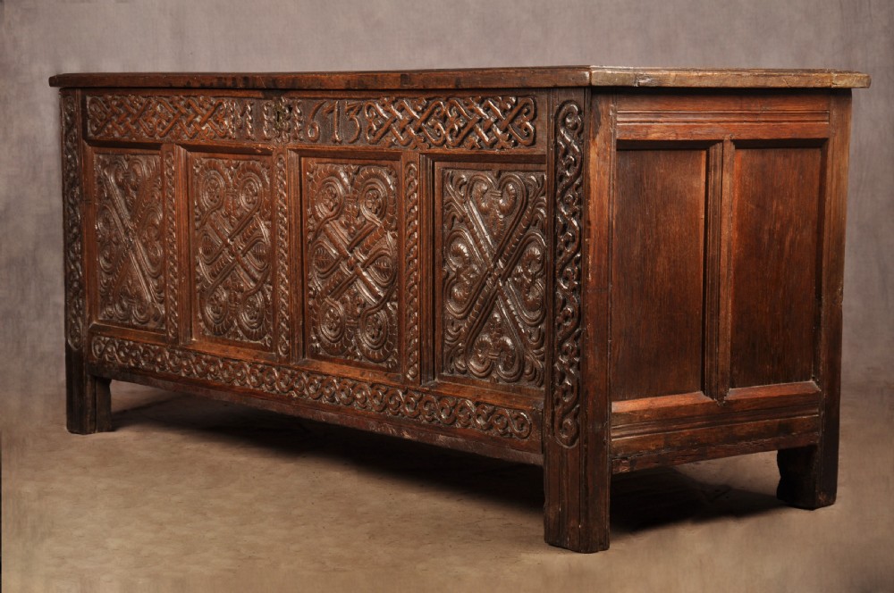 A dark oak 17th-century coffer featuring four carved relief panels, a carved top frieze with an inscribed date, and a hinged lid. View IX