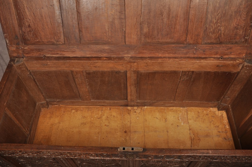 A dark oak 17th-century coffer featuring four carved relief panels, a carved top frieze with an inscribed date, and a hinged lid. View X
