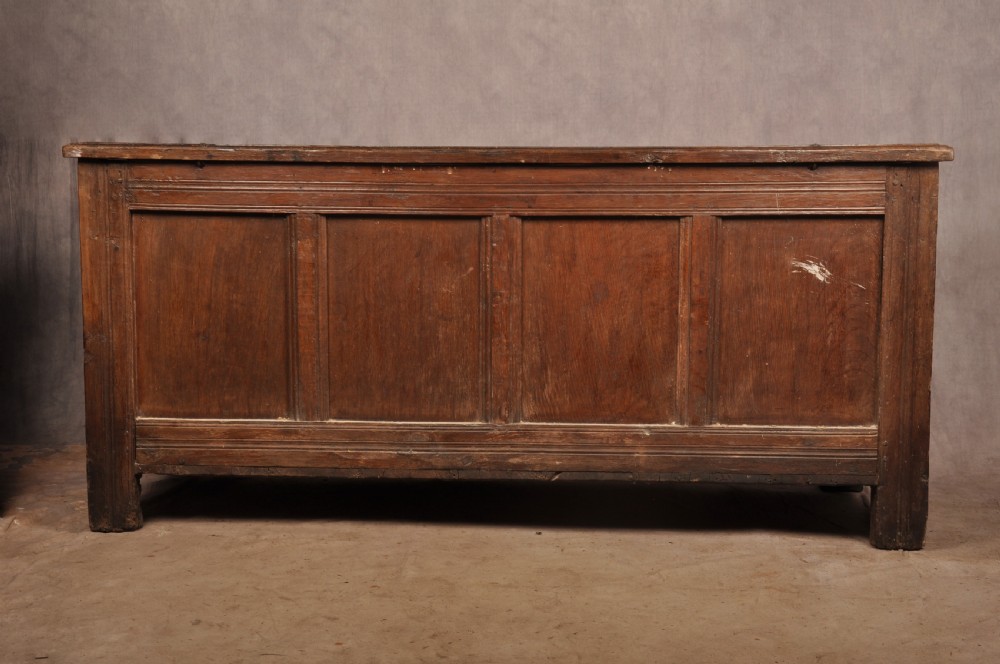 A dark oak 17th-century coffer featuring four carved relief panels, a carved top frieze with an inscribed date, and a hinged lid. View XIII
