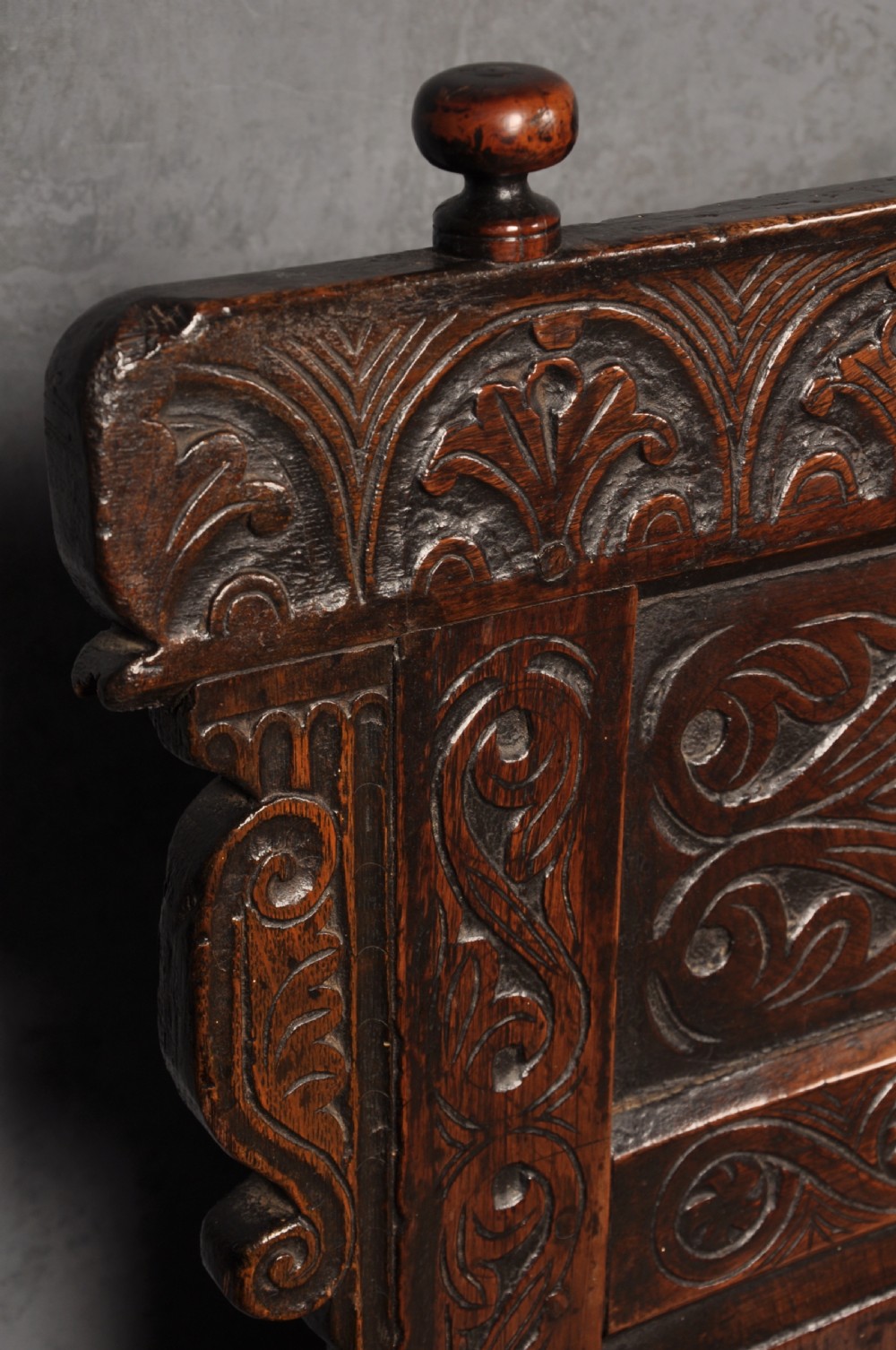 A 17th-century dark oak settle featuring a high carved panelled back with carved cresting and initials above a long bench seat with turned legs. View V