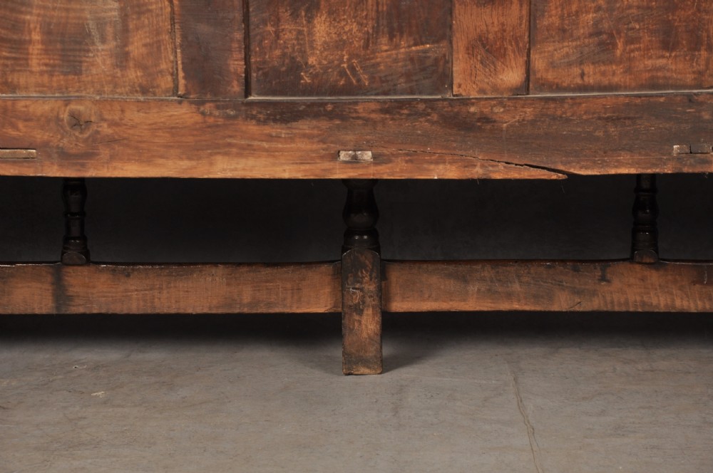A 17th-century dark oak settle featuring a high carved panelled back with carved cresting and initials above a long bench seat with turned legs. View XII