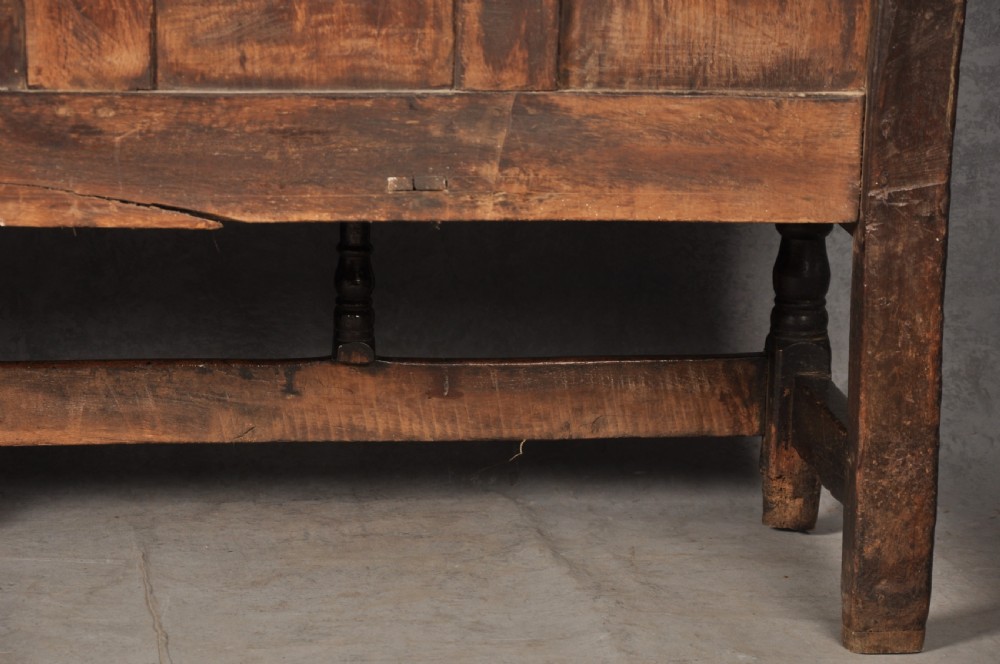 A 17th-century dark oak settle featuring a high carved panelled back with carved cresting and initials above a long bench seat with turned legs. View XIII