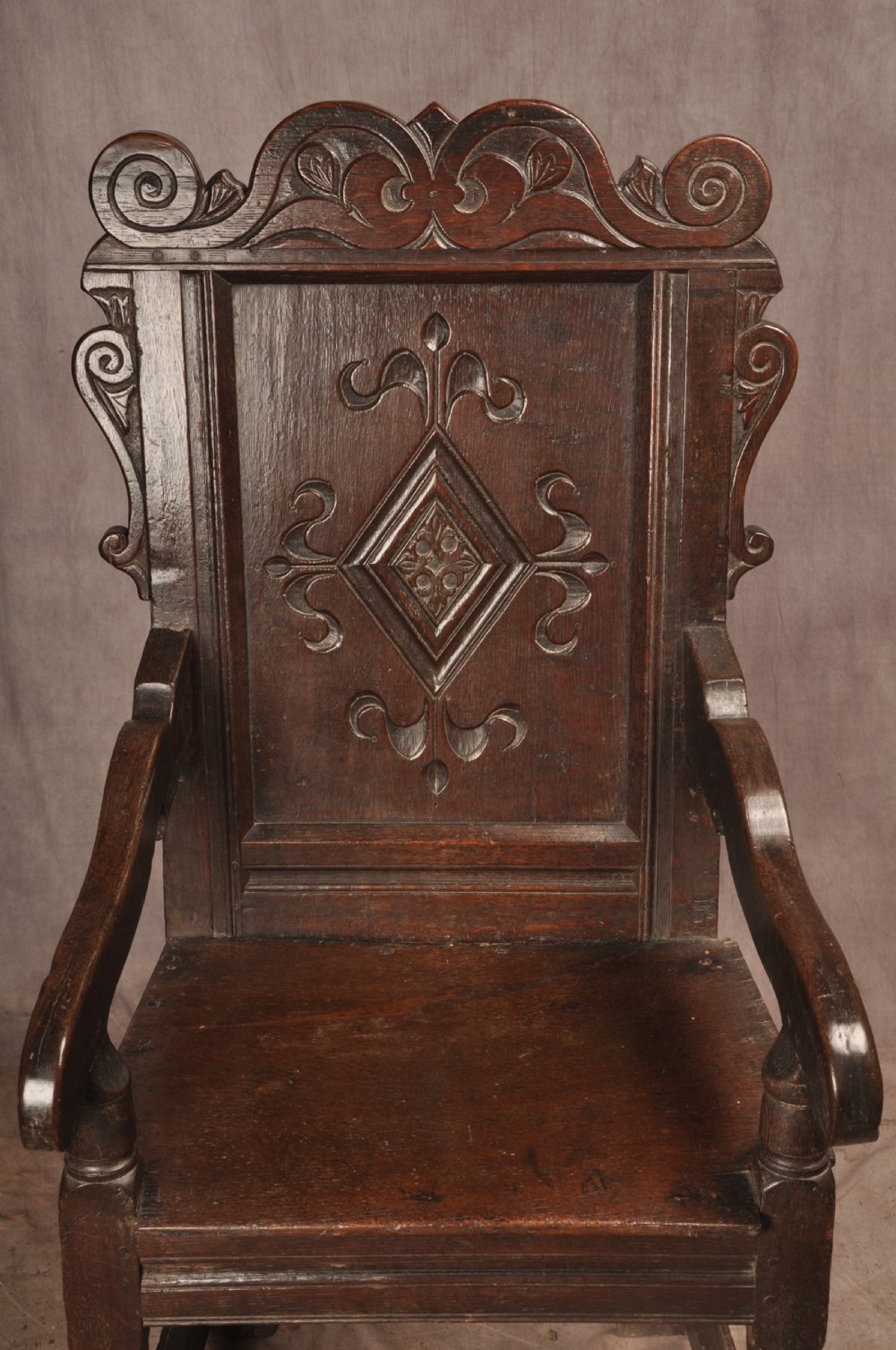 A 17th-century dark oak wainscot armchair featuring a carved scrolled cresting rail, a lozenge-carved back panel, turned front legs, and a solid wooden seat. View II