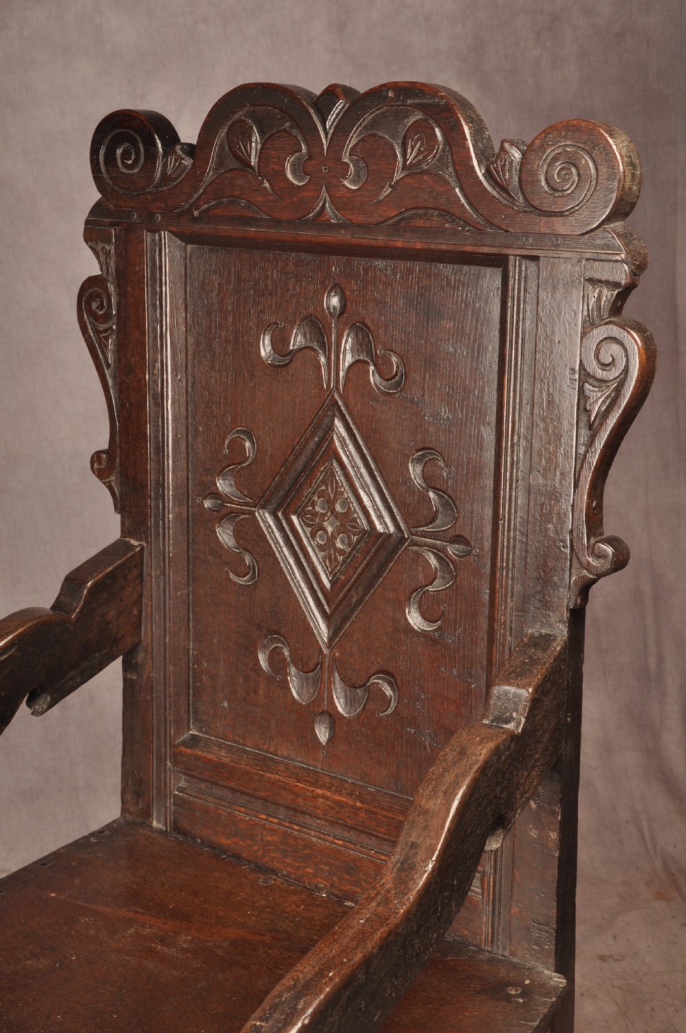 A 17th-century dark oak wainscot armchair featuring a carved scrolled cresting rail, a lozenge-carved back panel, turned front legs, and a solid wooden seat. View III