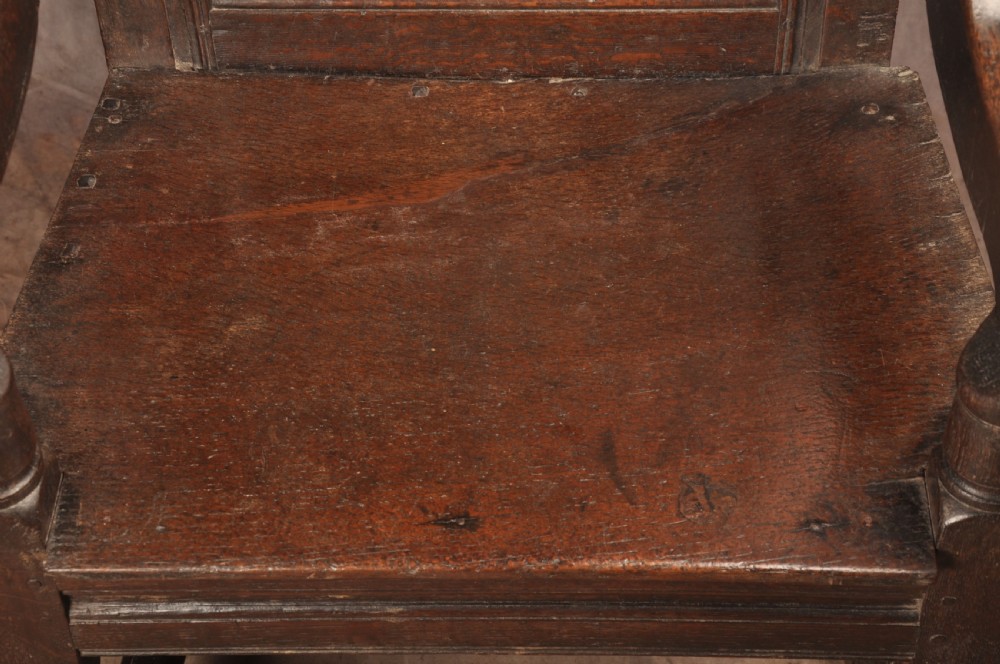 A 17th-century dark oak wainscot armchair featuring a carved scrolled cresting rail, a lozenge-carved back panel, turned front legs, and a solid wooden seat. View VI