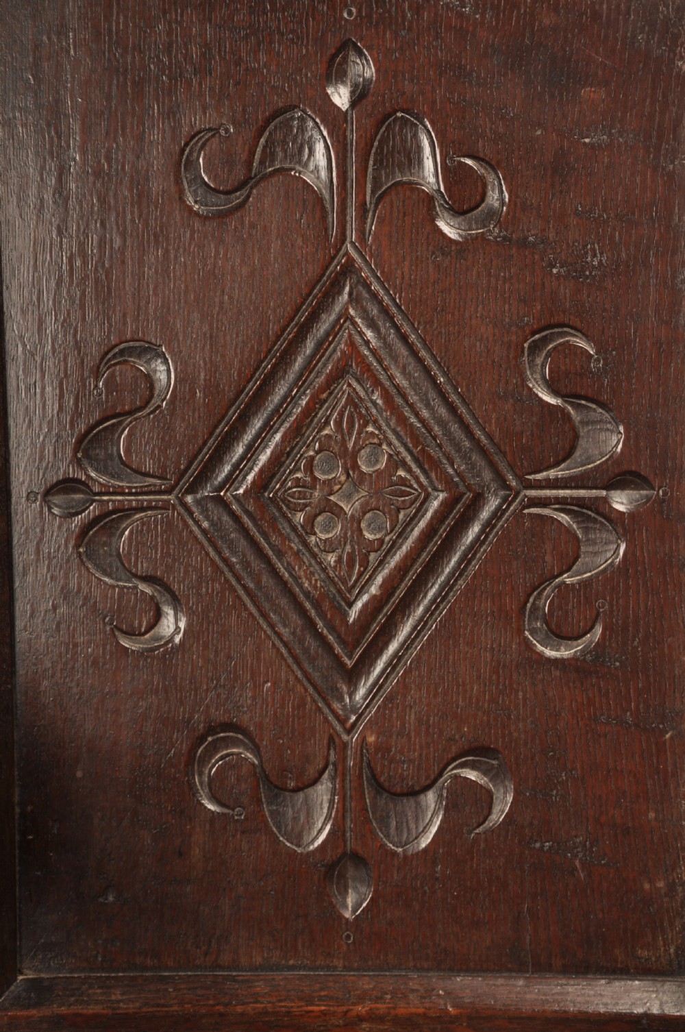 A 17th-century dark oak wainscot armchair featuring a carved scrolled cresting rail, a lozenge-carved back panel, turned front legs, and a solid wooden seat. View VII