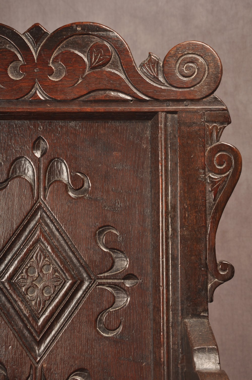 A 17th-century dark oak wainscot armchair featuring a carved scrolled cresting rail, a lozenge-carved back panel, turned front legs, and a solid wooden seat. View VIII