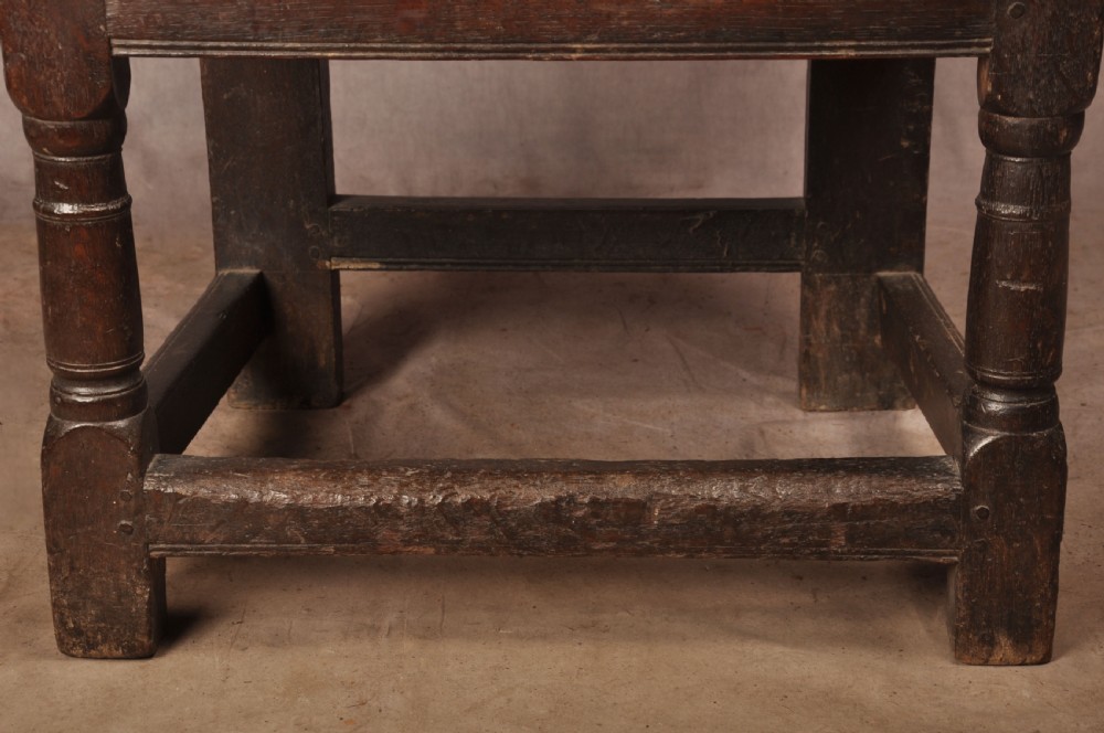 A 17th-century dark oak wainscot armchair featuring a carved scrolled cresting rail, a lozenge-carved back panel, turned front legs, and a solid wooden seat. View IX