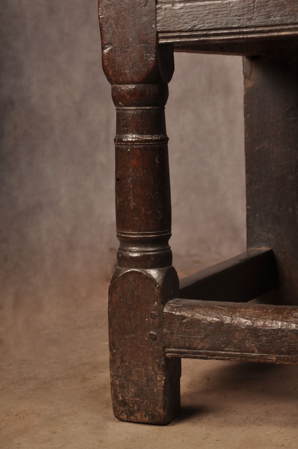 A 17th-century dark oak wainscot armchair featuring a carved scrolled cresting rail, a lozenge-carved back panel, turned front legs, and a solid wooden seat. View X
