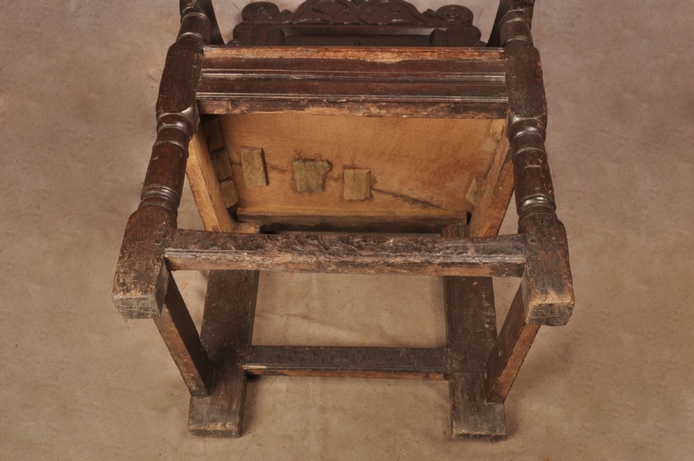 A 17th-century dark oak wainscot armchair featuring a carved scrolled cresting rail, a lozenge-carved back panel, turned front legs, and a solid wooden seat. View XII