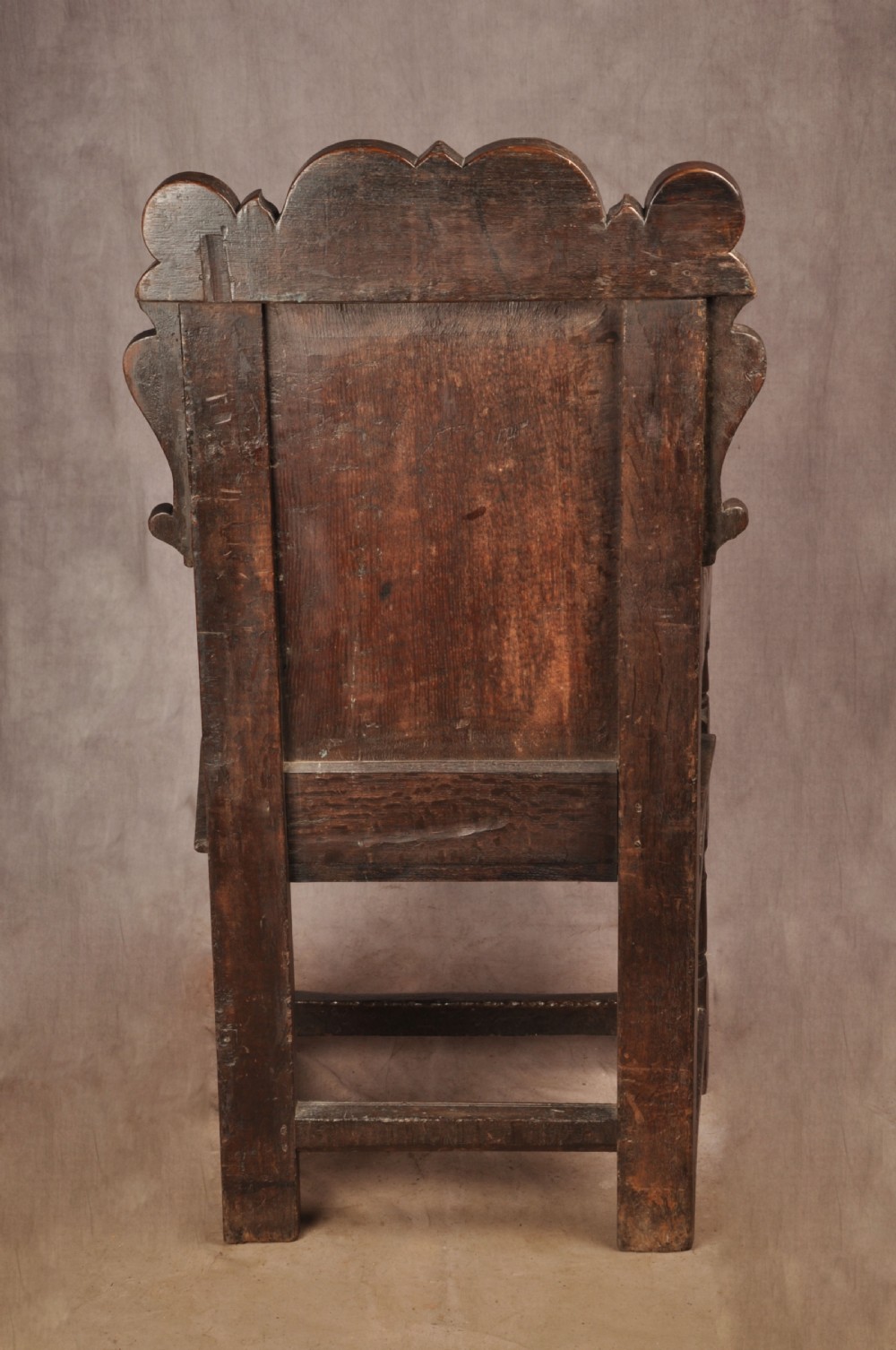 A 17th-century dark oak wainscot armchair featuring a carved scrolled cresting rail, a lozenge-carved back panel, turned front legs, and a solid wooden seat. View XIII