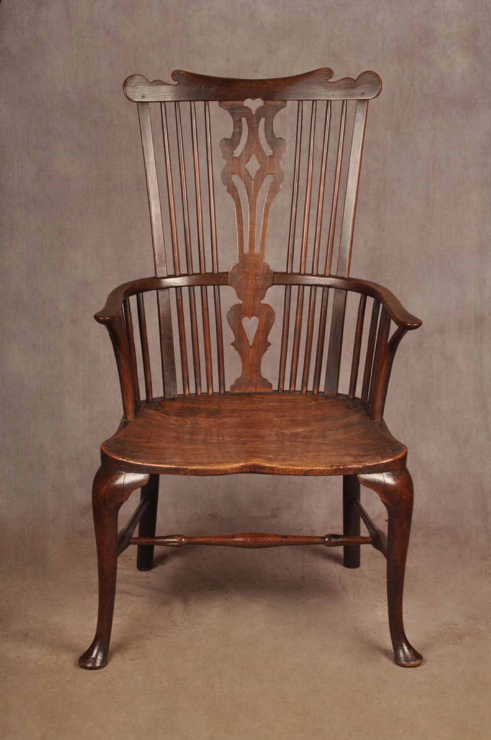 An 18th-century cherrywood Thames Valley Windsor armchair featuring a high comb back, pierced fretwork splat, curved armrests, saddled seat, and cabriole front legs.