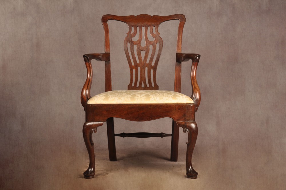 A George II mahogany armchair featuring a pierced back splat, swept armrests, a cream fabric seat, and cabriole front legs.