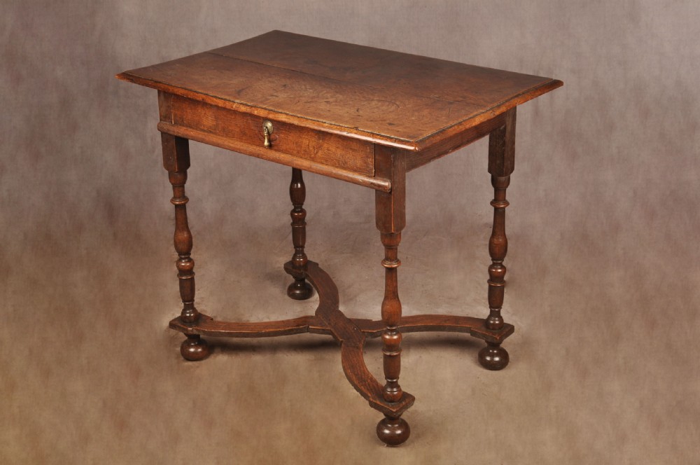 A 17th-century oak side table featuring baluster-turned legs, a shaped X-stretcher, a single frieze drawer with a brass drop handle, and a rectangular timber top.