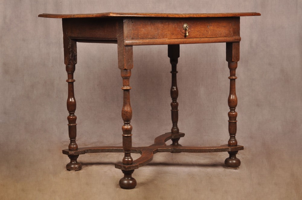 A 17th-century oak side table featuring baluster-turned legs, a shaped X-stretcher, a single frieze drawer with a brass drop handle, and a rectangular timber top. View V