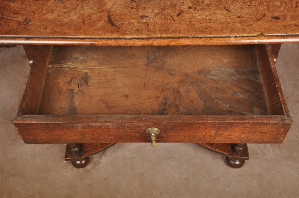 A 17th-century oak side table featuring baluster-turned legs, a shaped X-stretcher, a single frieze drawer with a brass drop handle, and a rectangular timber top. View IX